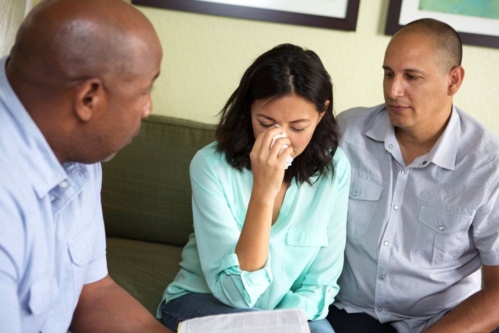 A Woman is Crying While Sitting on a Couch With Two Men — Living Well Psychology Clinic in Erina, NSW