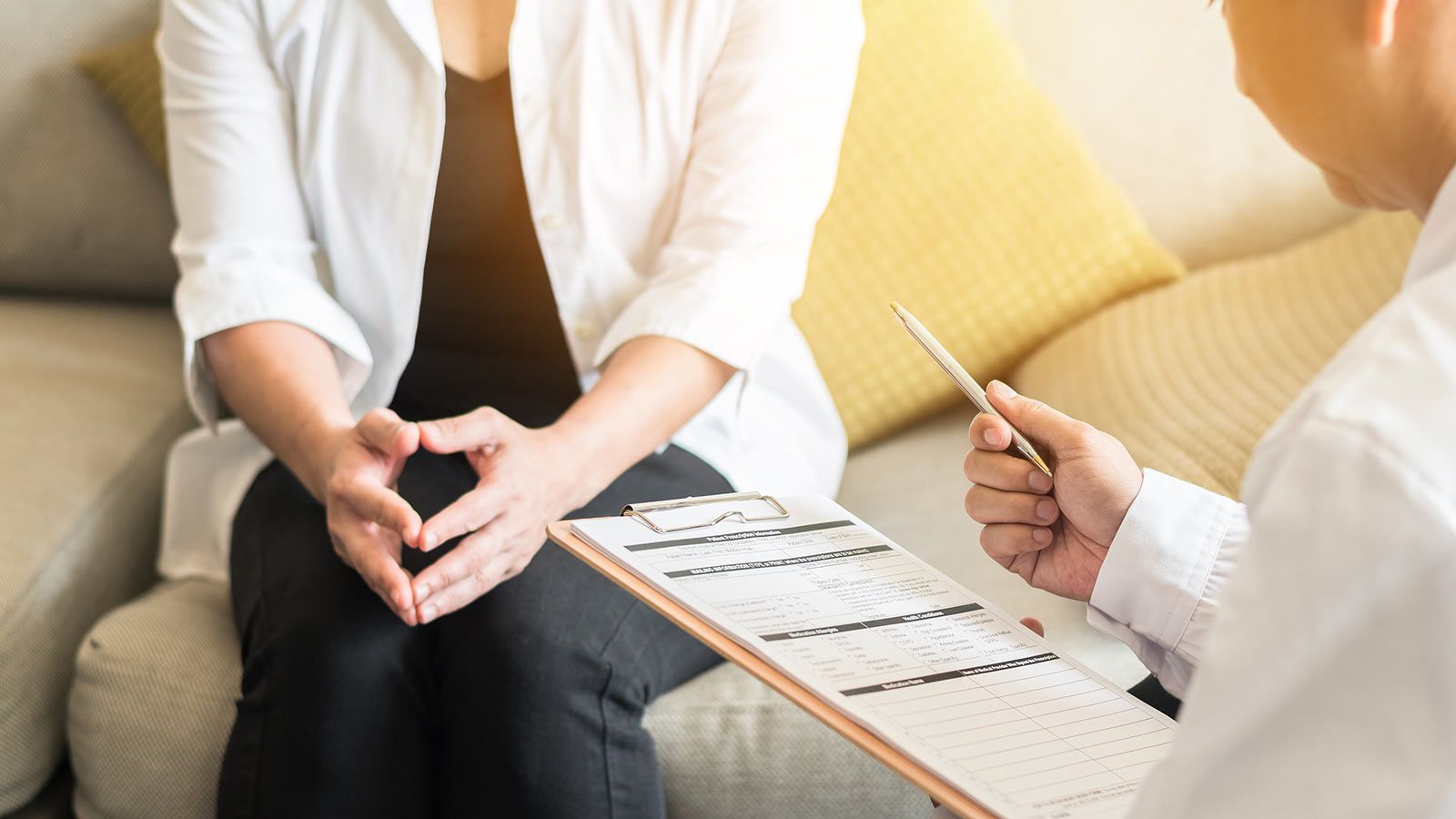 A Woman is Sitting on a Couch Talking to a Doctor While Holding a Clipboard — Living Well Psychology Clinic in Erina, NSW