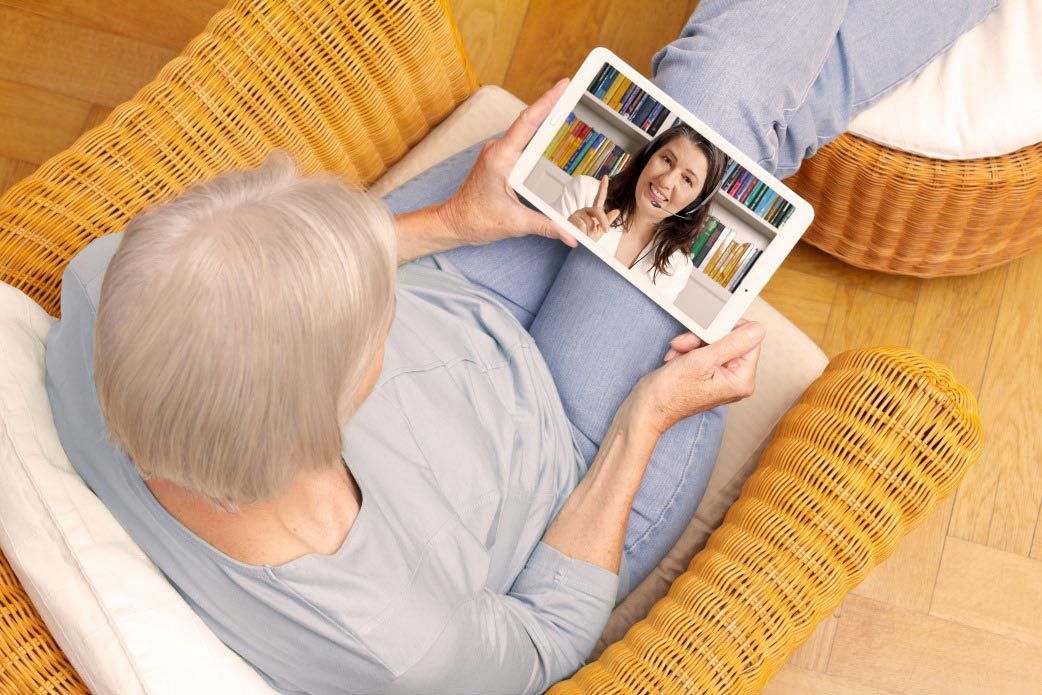 An Elderly Woman is Sitting in a Chair Using a Tablet Computer — Living Well Psychology Clinic in Erina, NSW