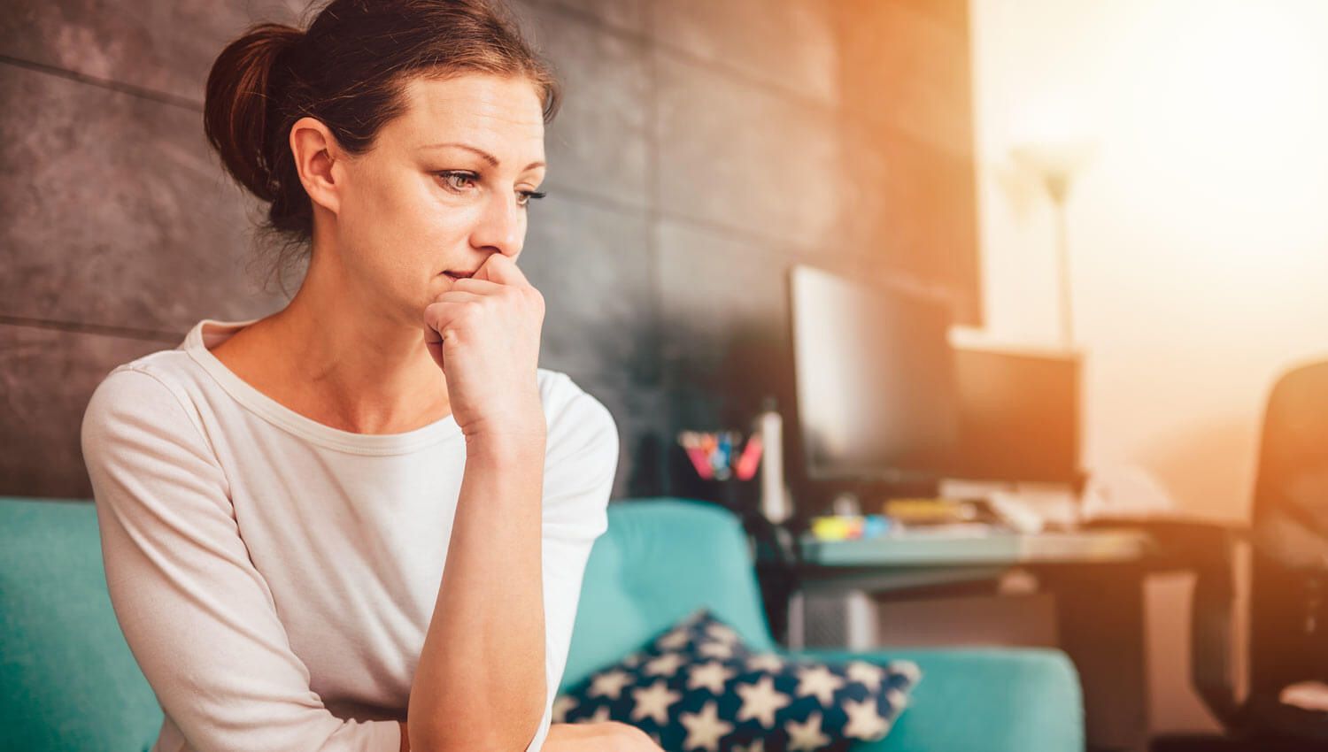 A Woman is Sitting on a Couch With Hand on Her Chin — Living Well Psychology Clinic in Erina, NSW