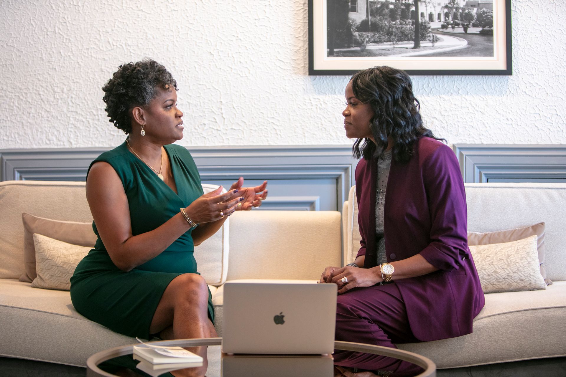 Two consultants are sitting at a table talking to each other. are sitting on a couch talking to each other while looking at a laptop.