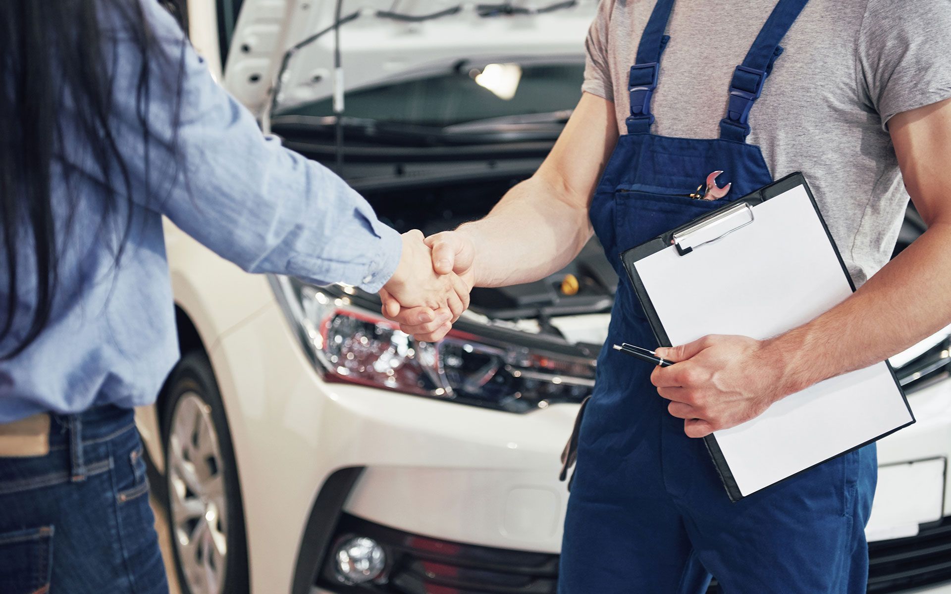A mechanic is shaking hands with a woman in front of a car.