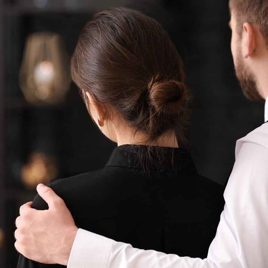 A person in a white shirt places a hand on the shoulder of another person in a dark shirt.