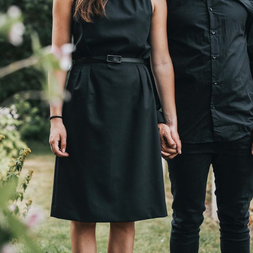 A couple dressed in black clothing hold hands while standing in a grassy, outdoor setting.