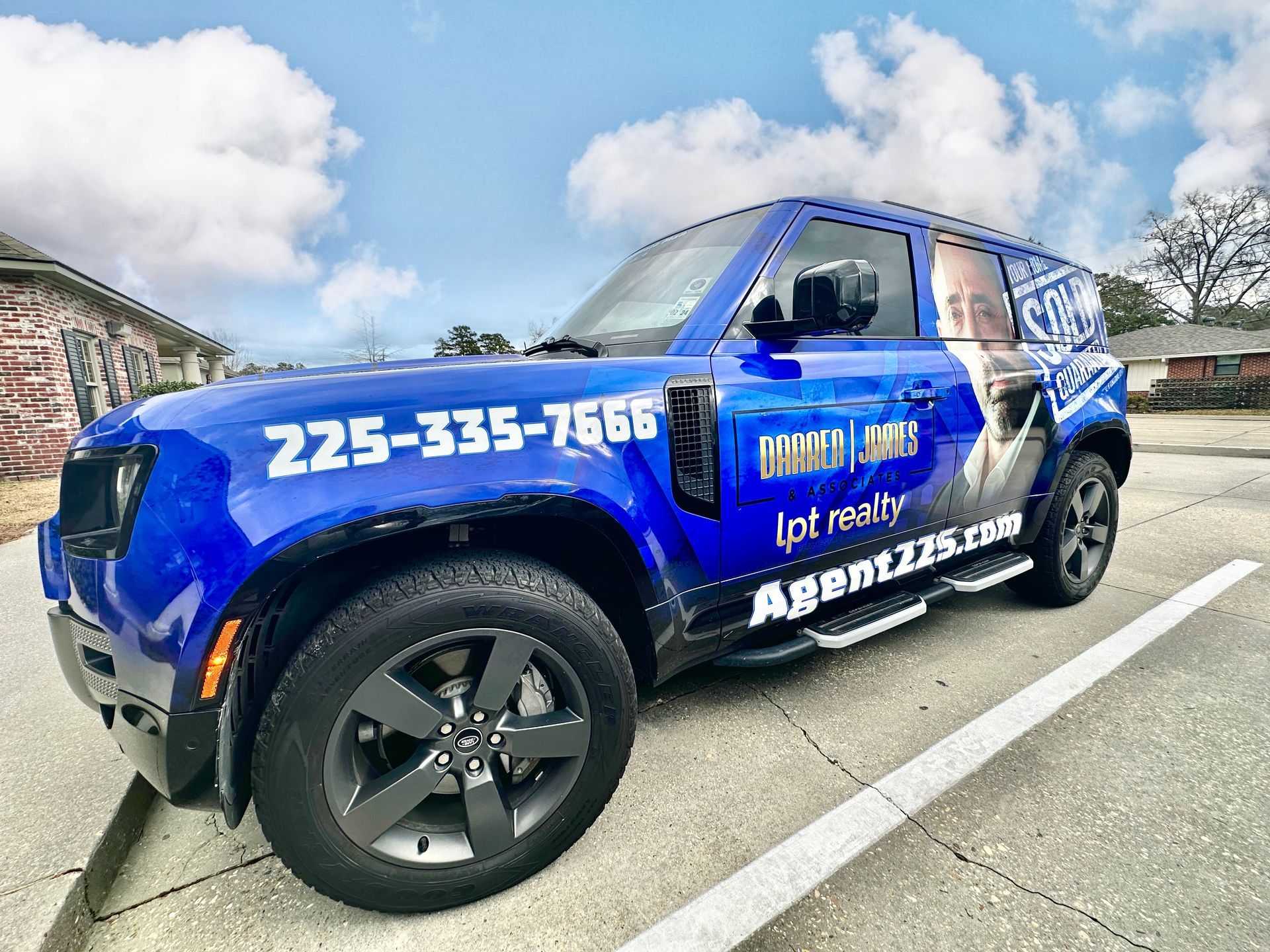 a blue land rover defender is parked in a parking lot . Darren James wrapped real estate vehicle