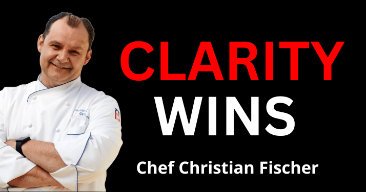 A chef with his arms crossed in front of a sign that says clarity wins