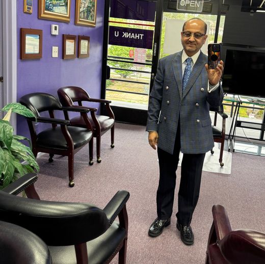 Man in suit holds a phone in a waiting room. He stands in front of chairs and a window with a 