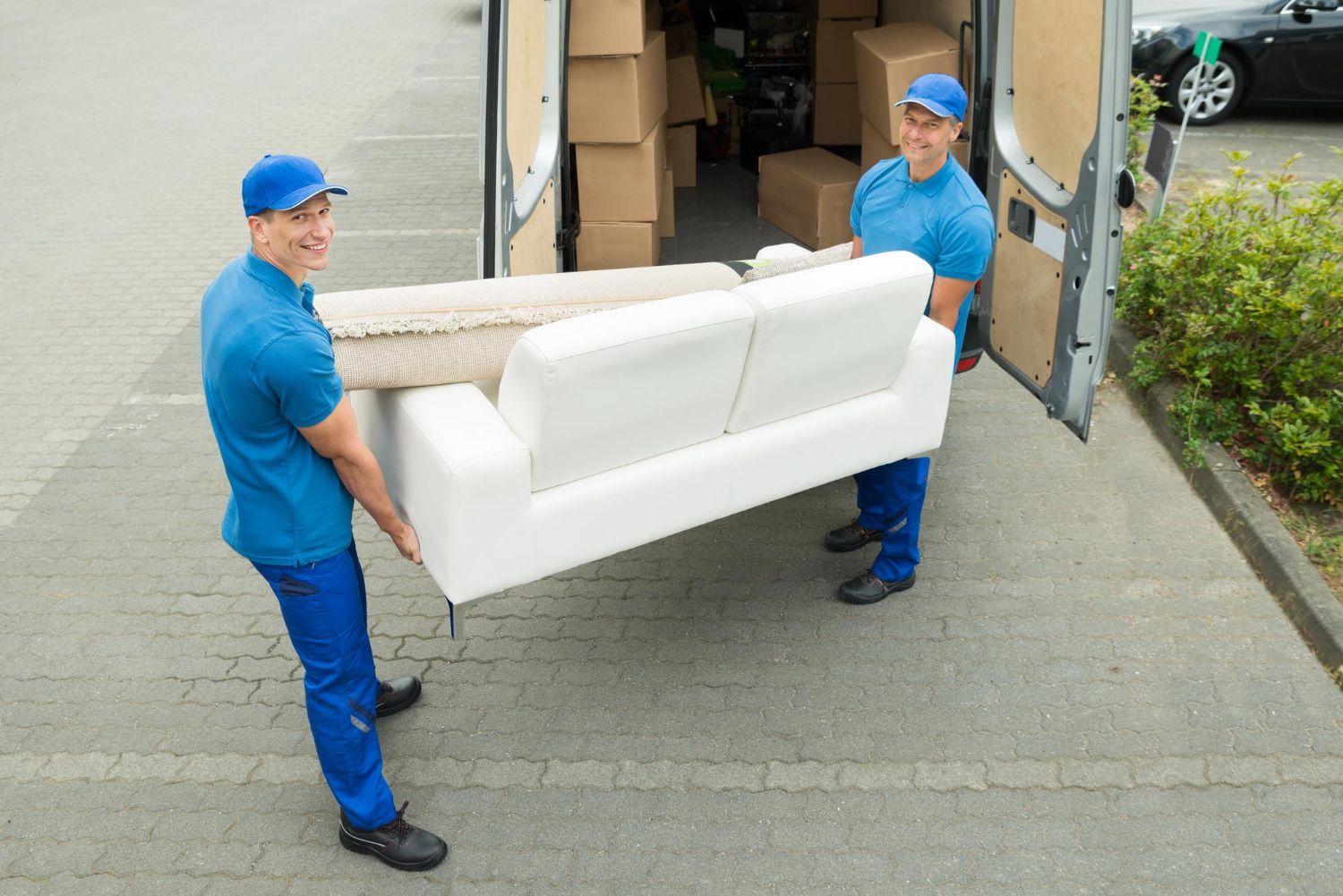 Two men are carrying a white couch out of a van.