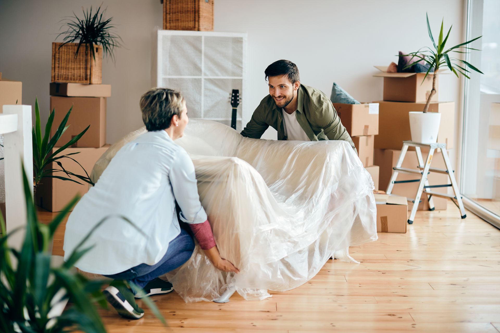A man and a woman are wrapping a couch in plastic while moving into a new home.