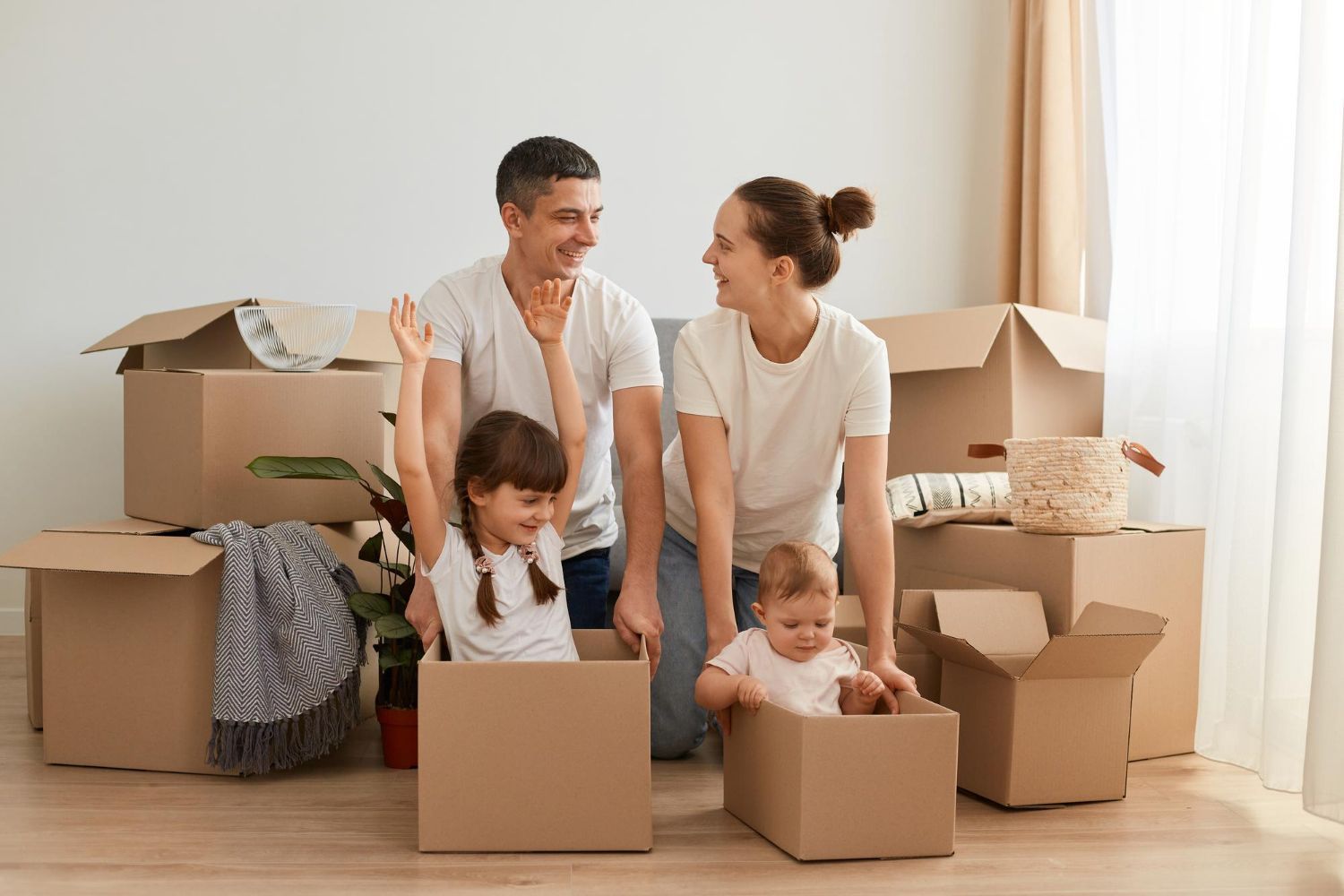A family is sitting in cardboard boxes in a living room.