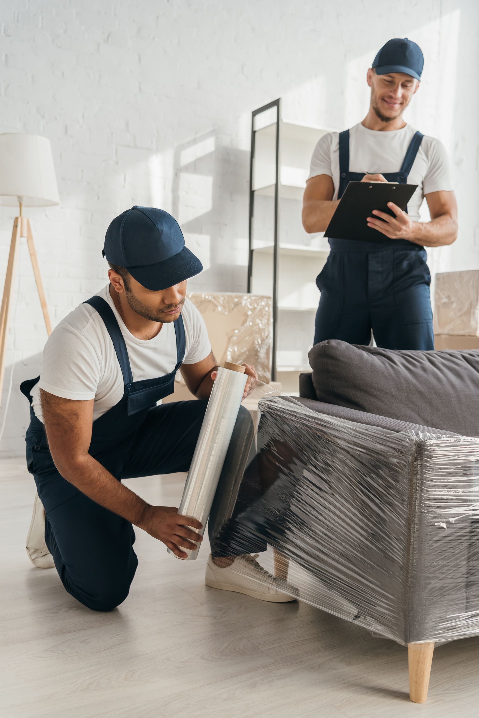 two men are wrapping a couch in plastic wrap in a living room .