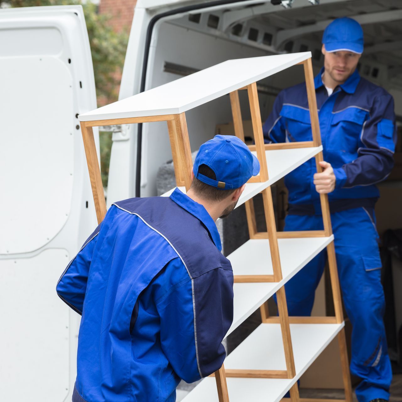 two men in blue uniforms are loading shelves into a van