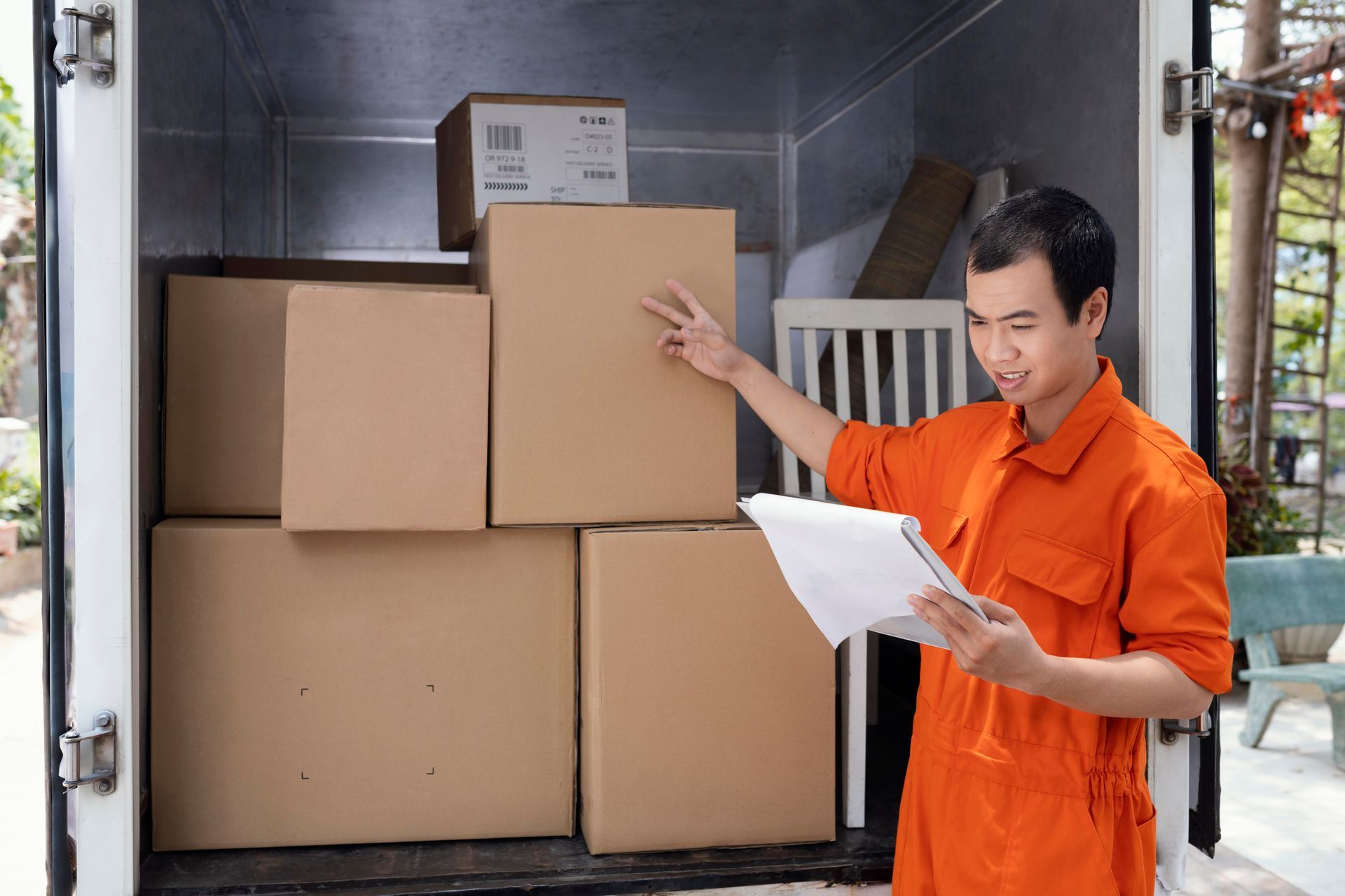 A man in an orange shirt is standing in front of a truck filled with cardboard boxes.