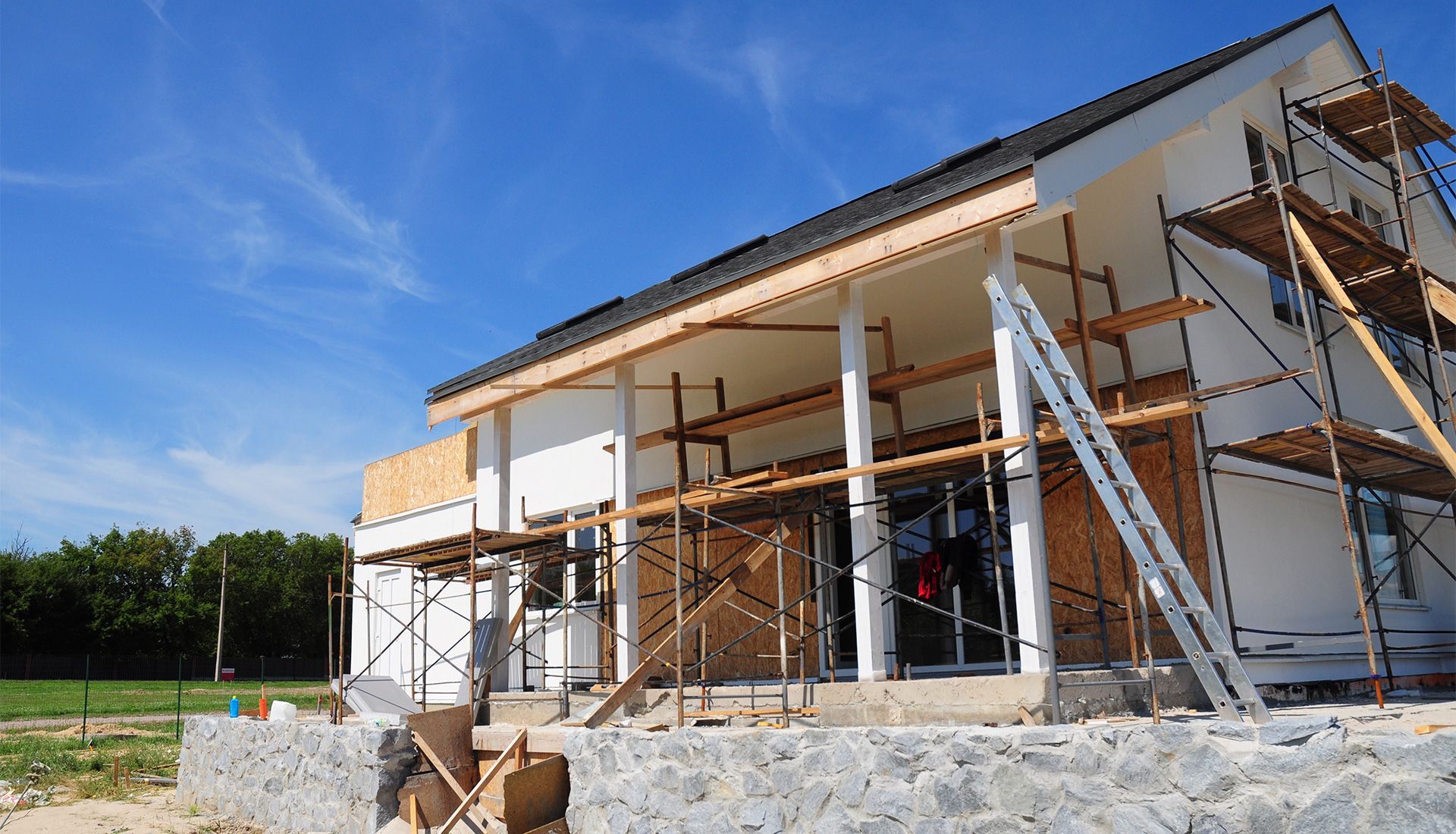 House under construction with scaffolding against a blue sky.