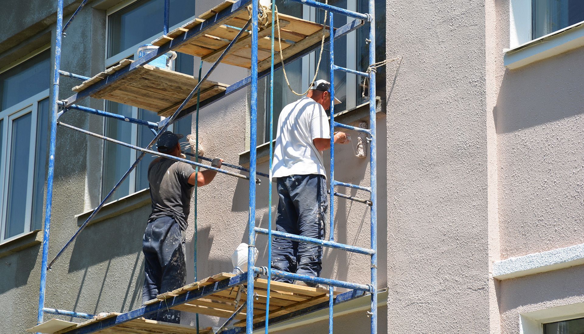 Two workers on scaffolding repairing a building's exterior wall.