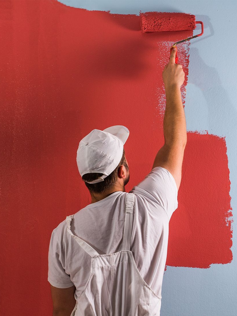 Person painting a wall red with a paint roller.