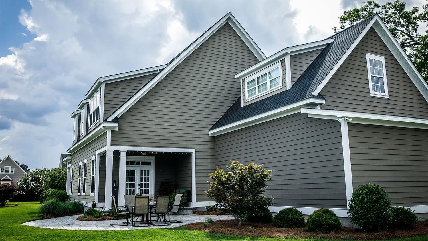 Gray house with white trim, patio, and lush landscaping on a cloudy day.