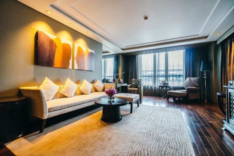 Luxury hotel living room with beige sofa, artwork, rug, and dark wood flooring.