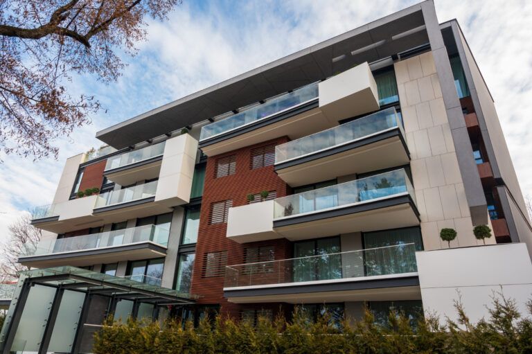 Modern apartment building with balconies, glass railings, and varied brick and concrete facade.