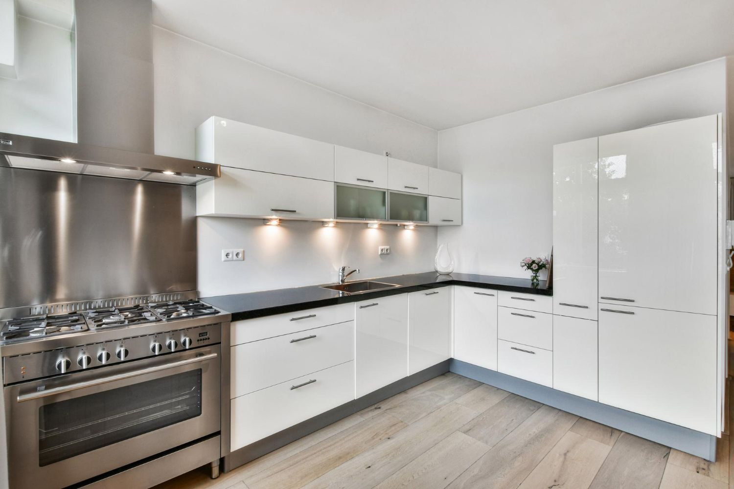Modern white kitchen with stainless steel appliances and wood floor.
