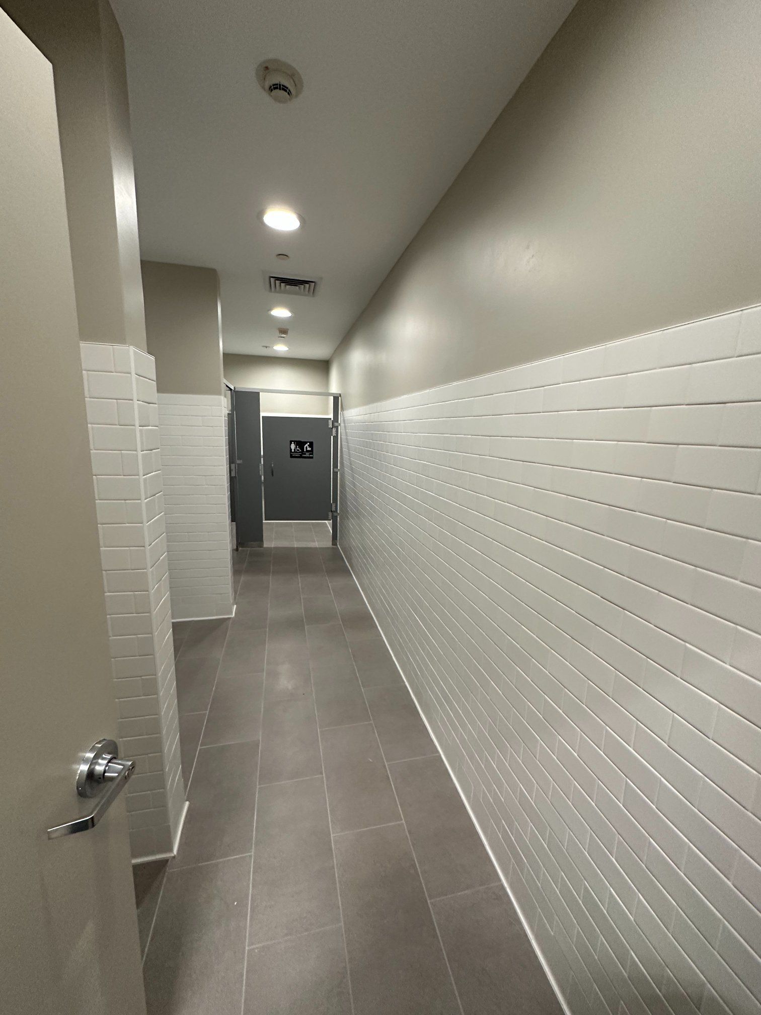 Narrow hallway with gray floor, white tiled wall, and closed gray doors.