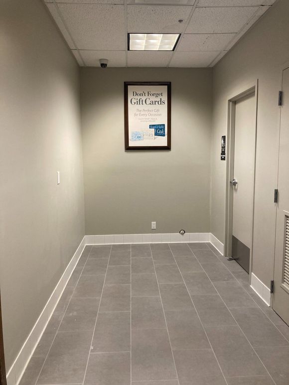 A hallway with light gray walls, a framed sign, a closed door, and gray tile flooring.