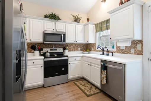 A kitchen with white cabinets , stainless steel appliances , a stove , microwave , and dishwasher.