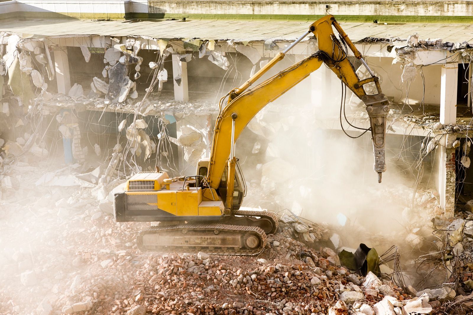 A yellow excavator is demolishing a building with a hammer.
