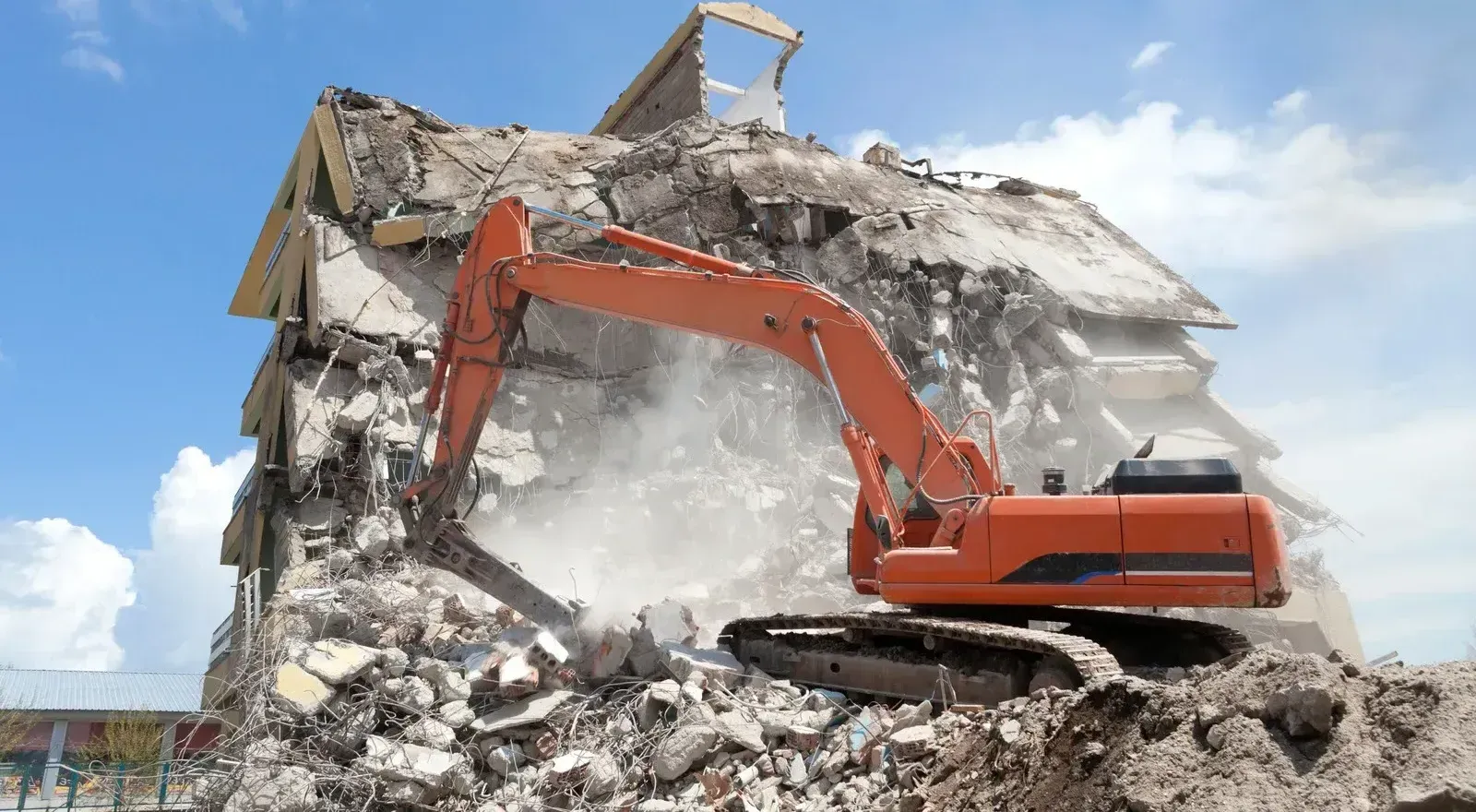 A large orange excavator is demolishing a building.