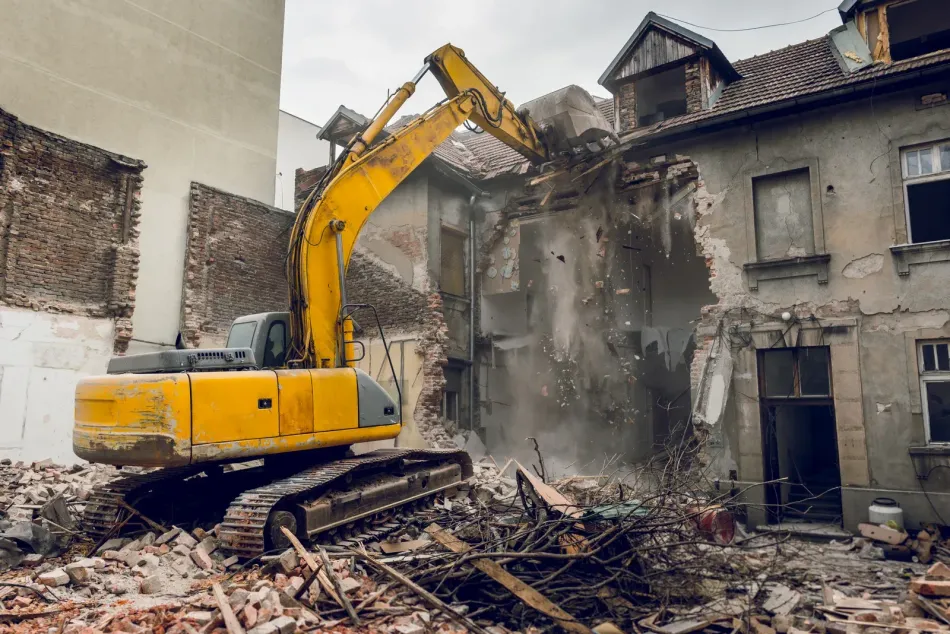 A yellow excavator is demolishing an old building.