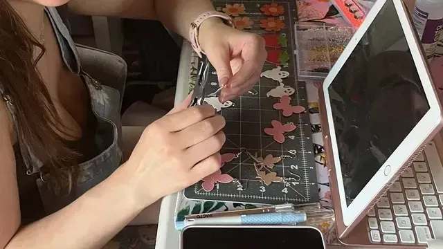 A woman is sitting at a desk making earrings.