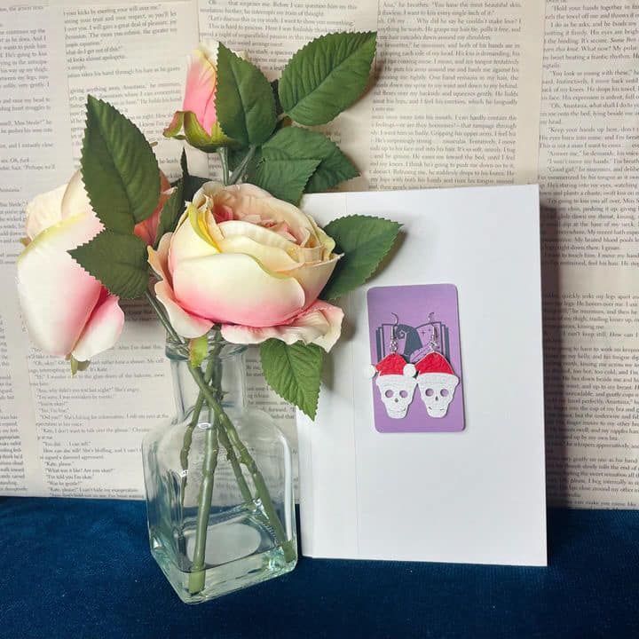 A card with skull earrings on it sits next to a vase of flowers