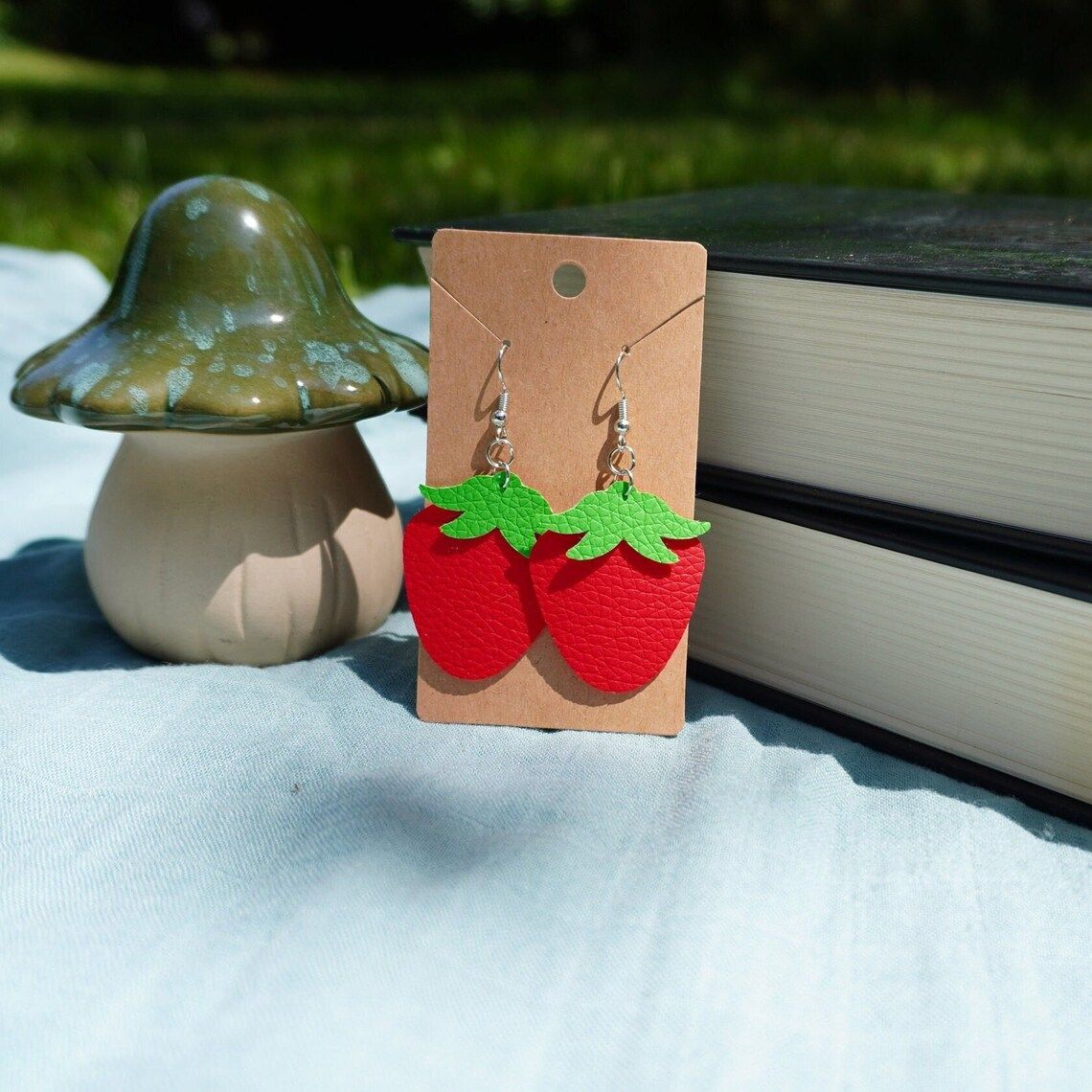 A pair of strawberry earrings on a card next to a mushroom