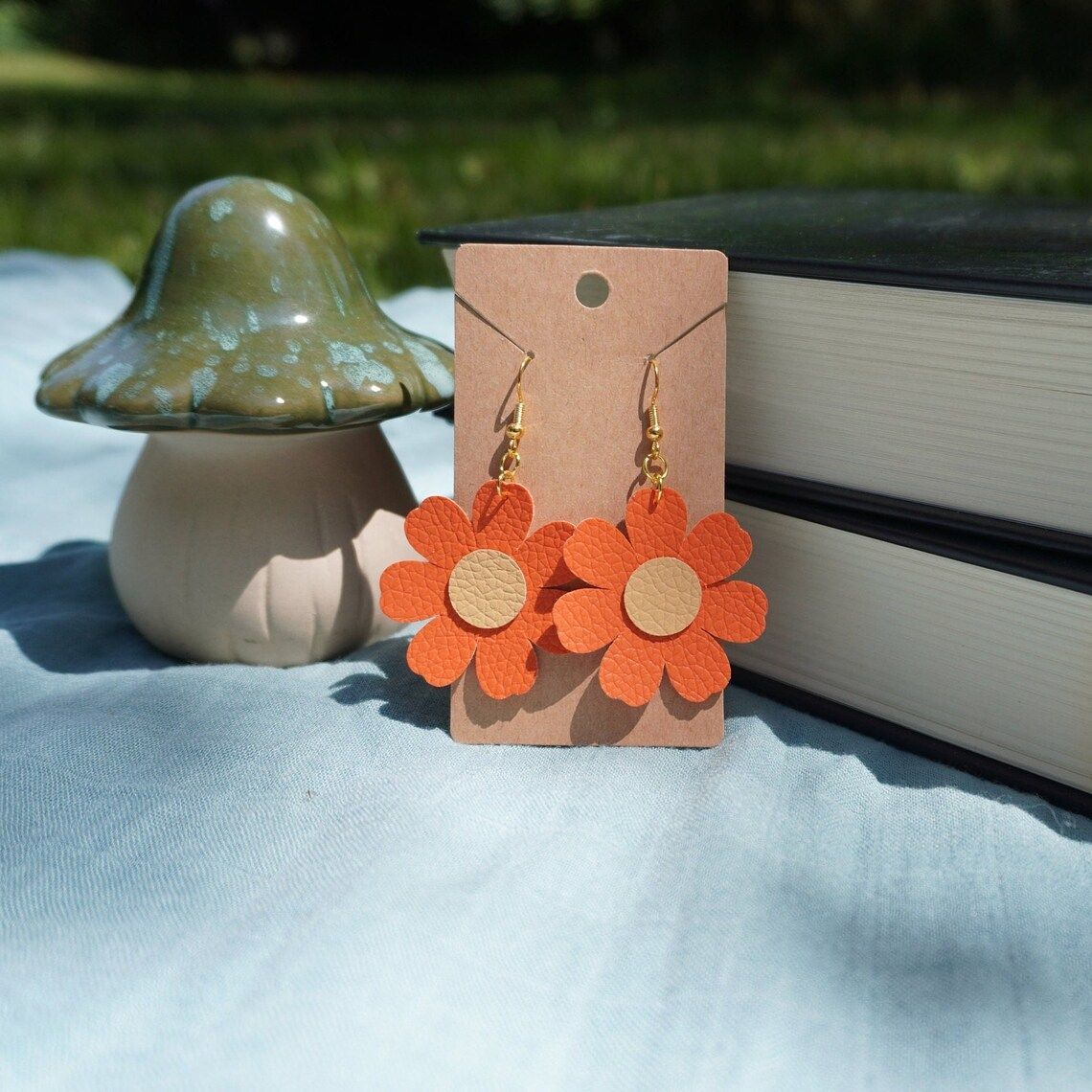 A pair of orange flower earrings on a card next to a mushroom and books