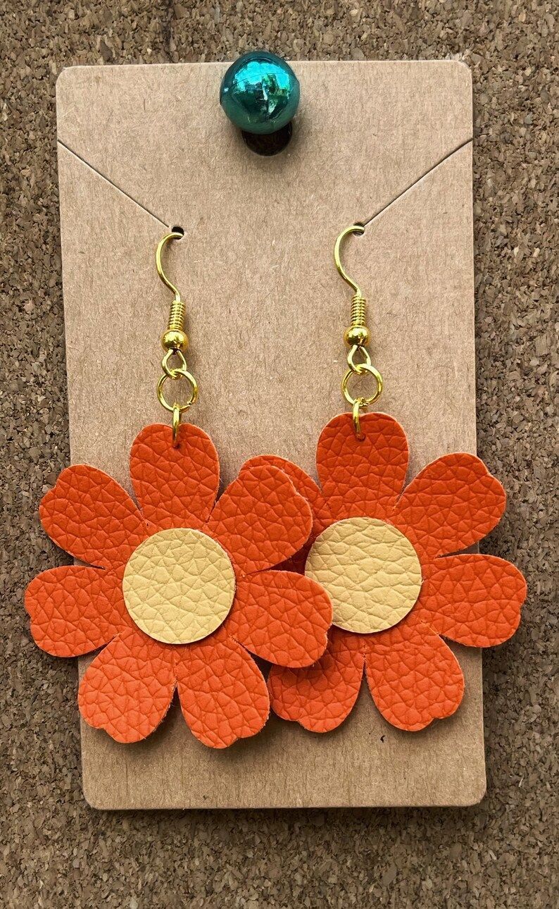 A pair of orange flower earrings on a card.