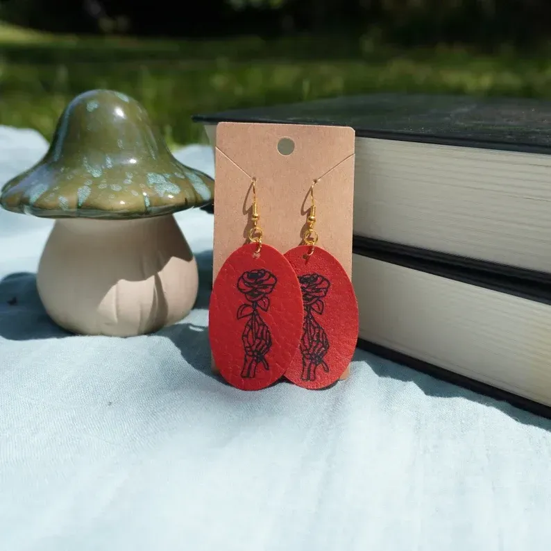 A pair of red earrings are on a card next to a mushroom and books