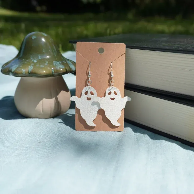 A pair of ghost earrings on a card next to a mushroom and books