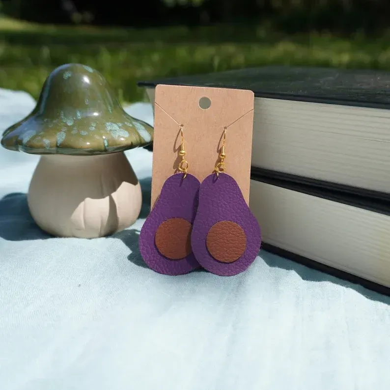 A pair of purple avocado shaped earrings on a card