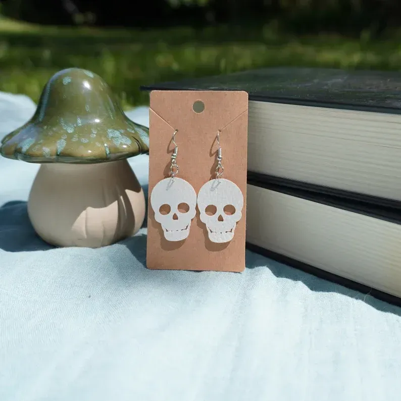 A pair of skull earrings on a card next to a mushroom and books