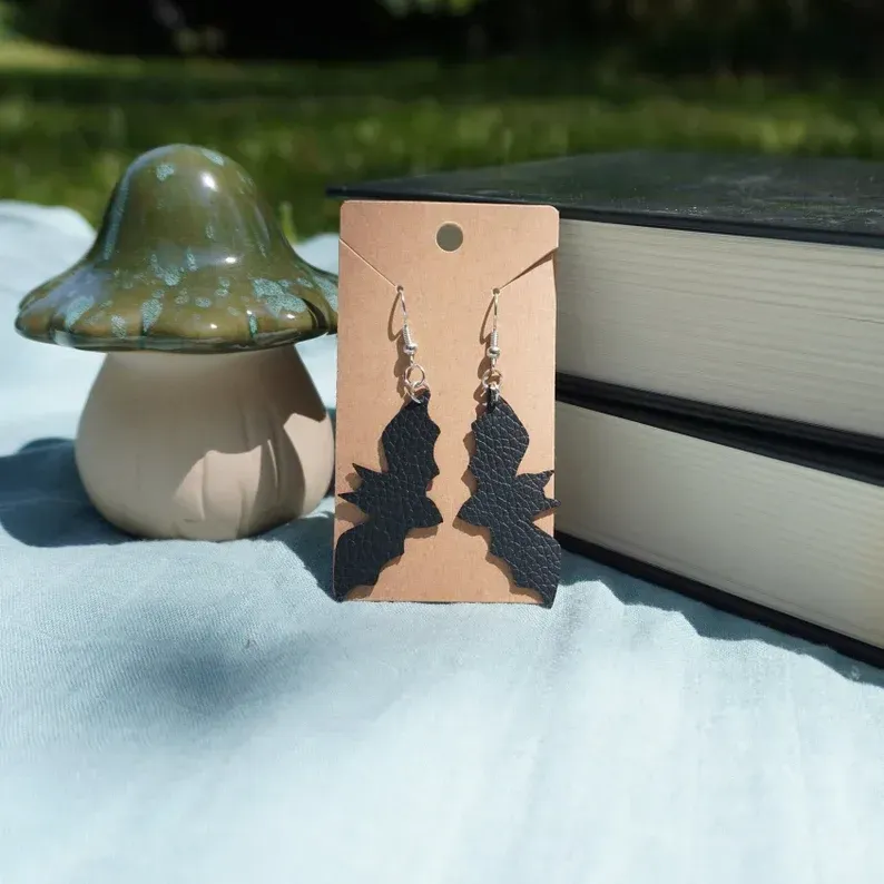 A pair of bat shaped earrings on a card next to a mushroom and books