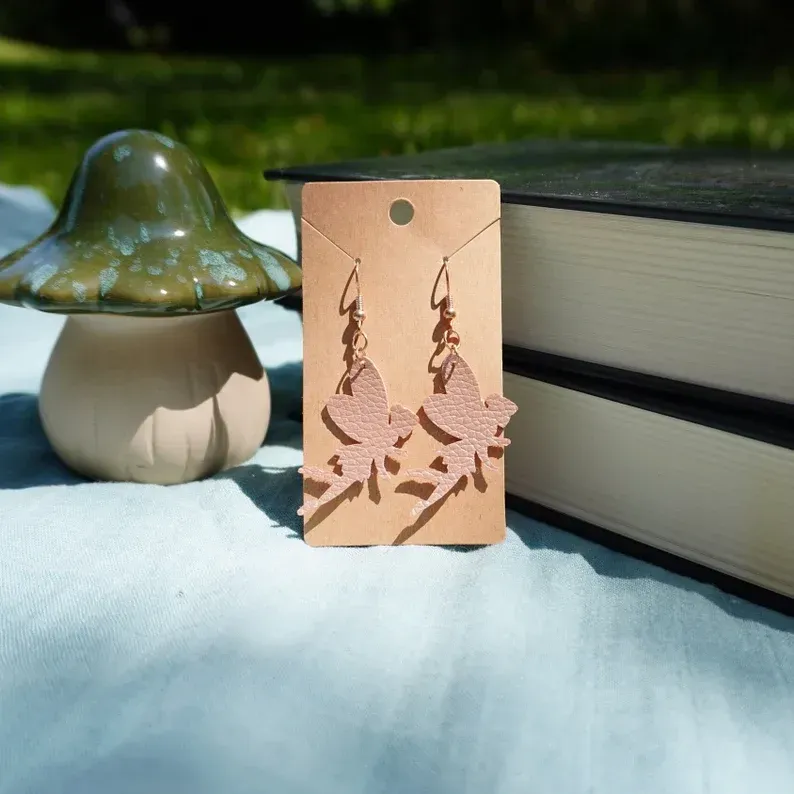 A pair of fairy earrings on a card next to a mushroom and books