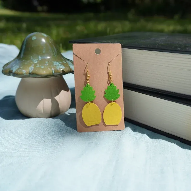 A pair of pineapple earrings on a card next to a mushroom and books