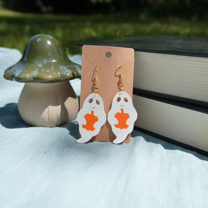 A pair of ghost earrings are on a card next to a mushroom and books