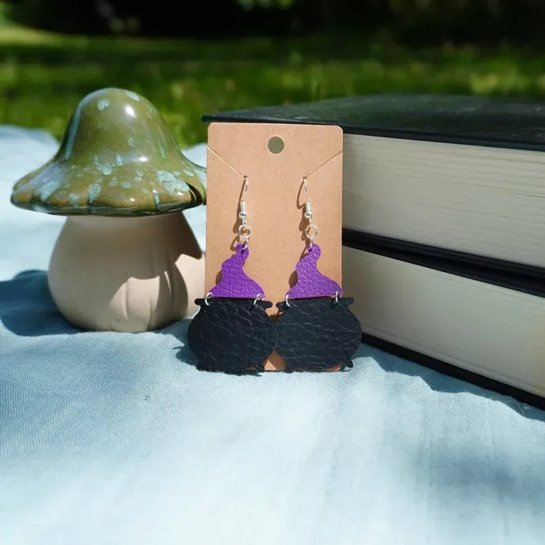A pair of purple and black witch cauldron earrings on a card