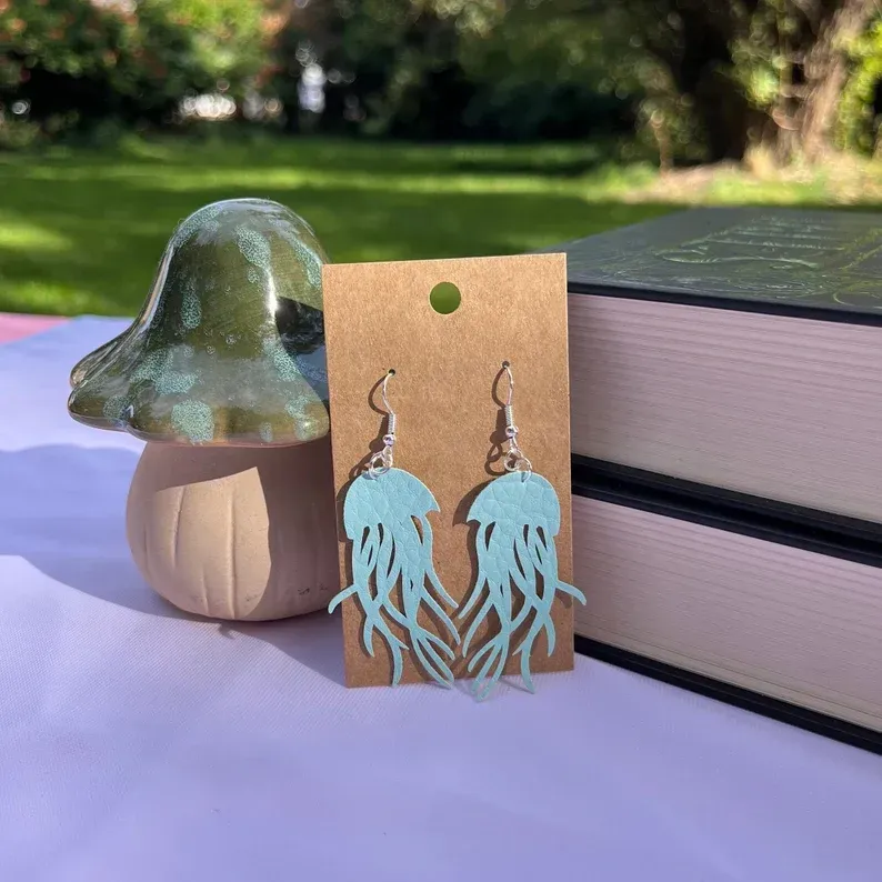 A pair of jellyfish earrings are sitting on a table next to a mushroom.