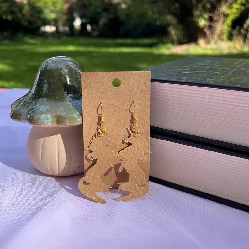 A pair of unicorn earrings are sitting on a table next to a mushroom and books.