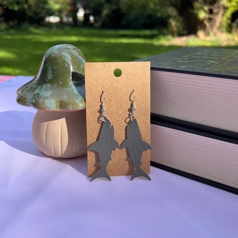A pair of shark earrings are sitting on a table next to a mushroom.