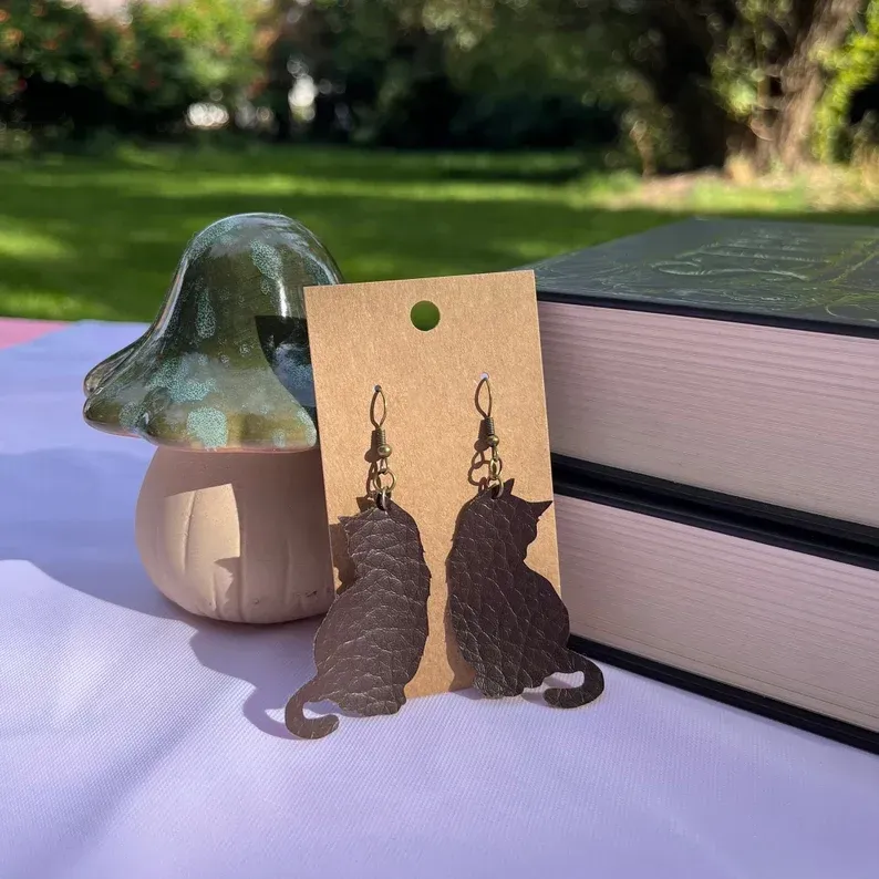A pair of cat earrings are sitting on a table next to a mushroom and books.