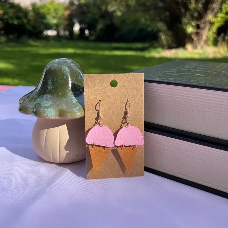 A pair of pink ice cream cone earrings are sitting on a table next to a mushroom.