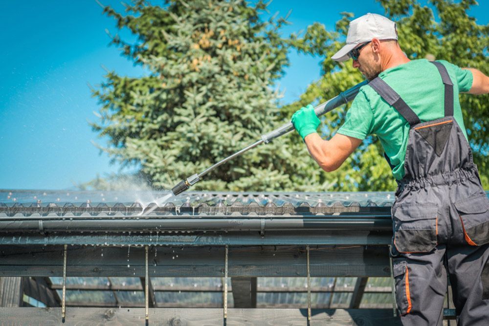 Man cleaning the roof gutter using water pressure — Handyman in Sussex Inlet, NSW